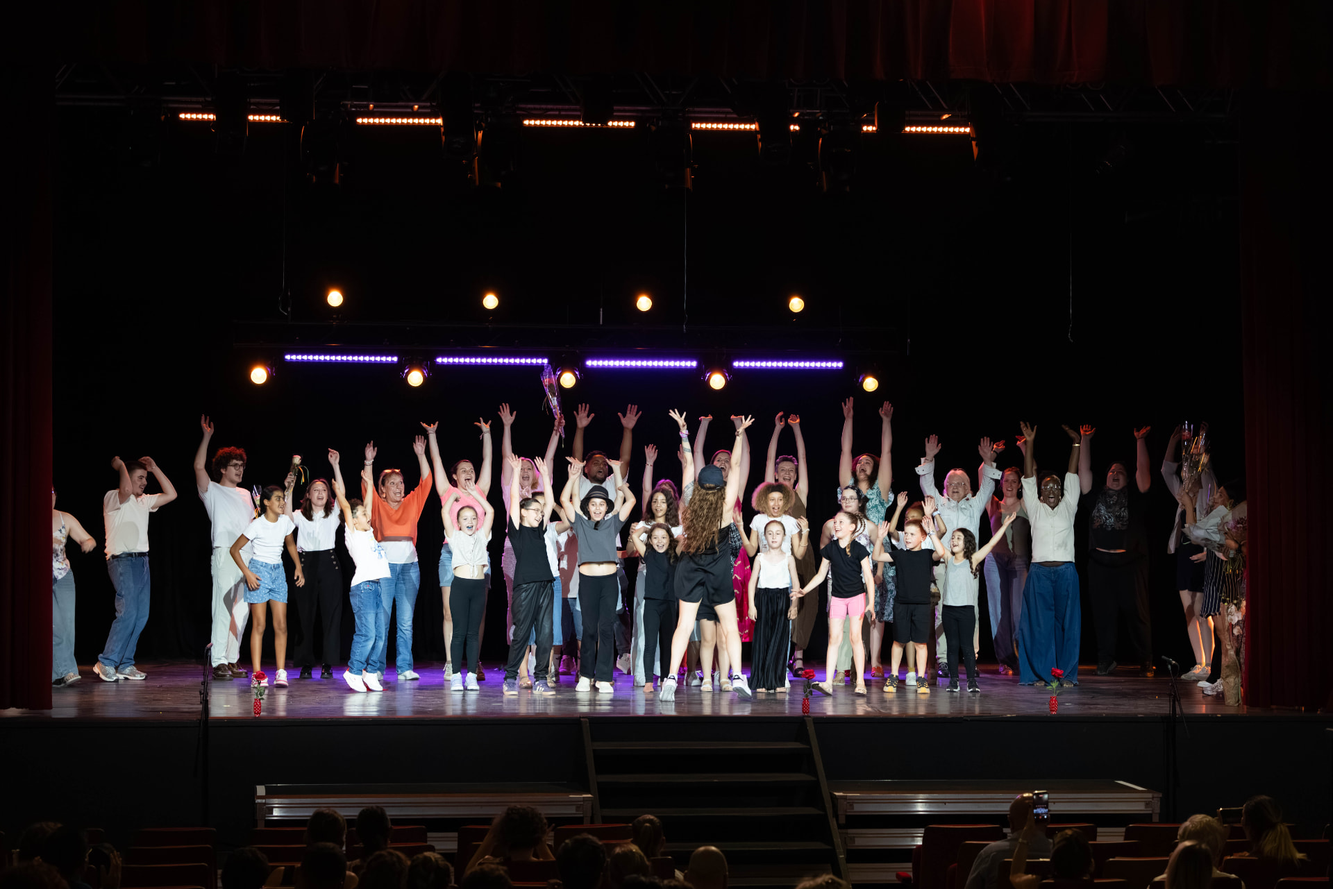 Un grand groupe d'adultes et d'enfants réunis sur scène, bras levés, à la fin d'un spectacle au Labo Théâtre